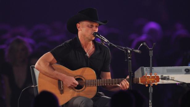 Ein Mann mit Cowboyhut spielt Gitarre und singt vor einem Publikum.