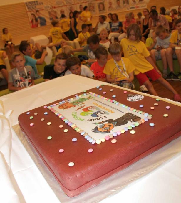 Ein großer, rechteckiger Kuchen mit dem Logo der „Kinder Business Week“ und bunten Süßigkeiten.