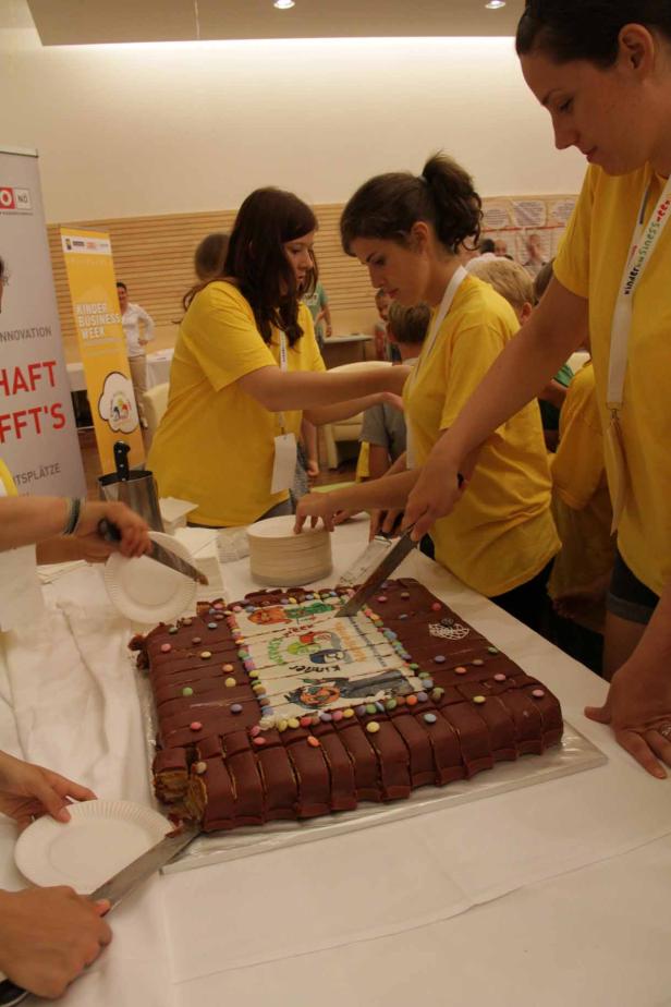 Mehrere Personen schneiden eine große, rechteckige Schokoladentorte an.