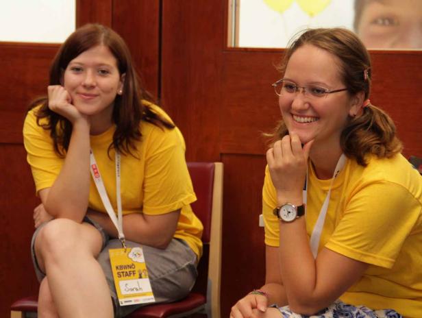 Zwei junge Frauen, vermutlich Mitarbeiterinnen, sitzen lächelnd nebeneinander.