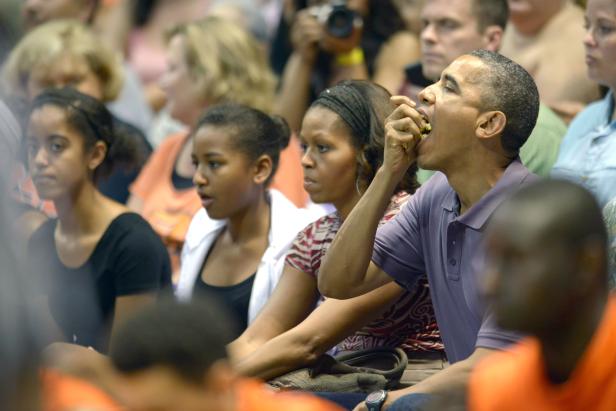 Barack Obama isst, während Michelle und ihre Töchter neben ihm sitzen.