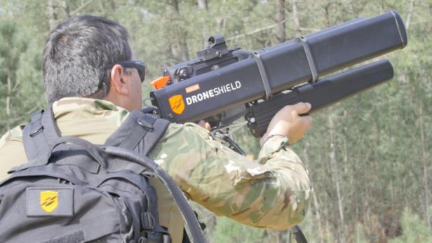 Ein Mann in Militärkleidung zielt mit einem DroneShield-Gerät in einer bewaldeten Umgebung.