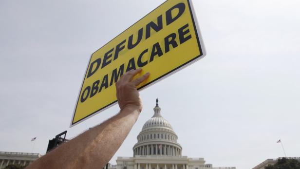 Eine Person hält ein Schild mit der Aufschrift „Defund Obamacare“ vor dem Kapitol der Vereinigten Staaten.
