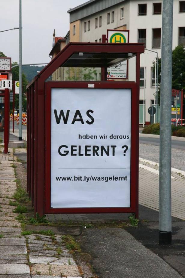 Ein rotes Bushaltestellenschild mit der Aufschrift „WAS haben wir daraus GELERNT?“.