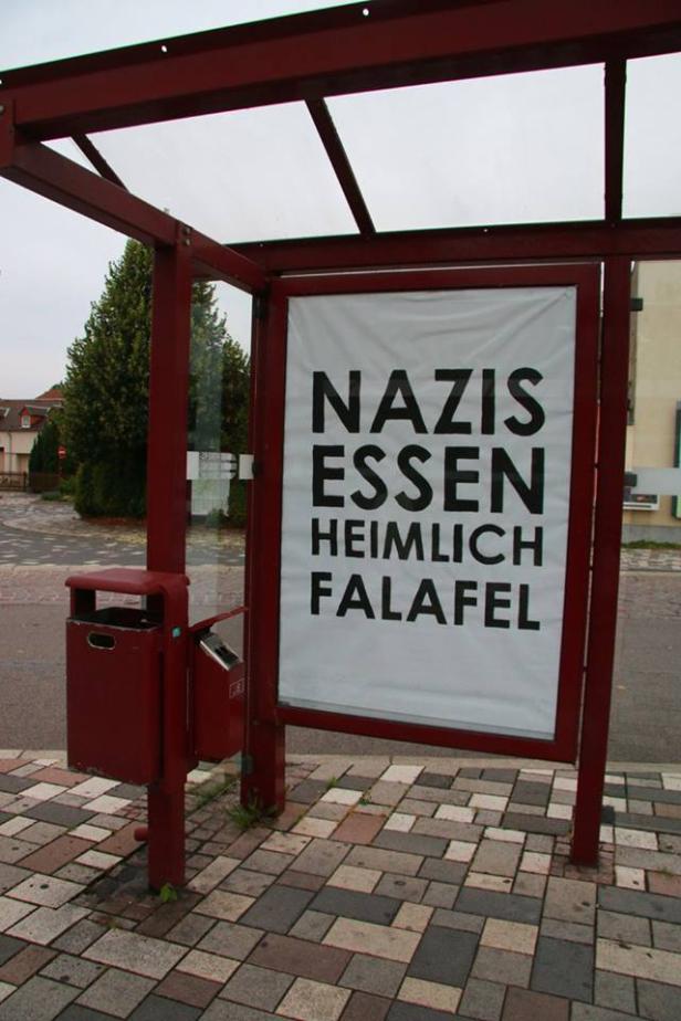 An einer Bushaltestelle hängt ein Plakat mit der Aufschrift „Nazis essen heimlich Falafel“.