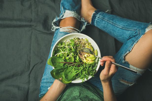Eine Frau isst einen Salat mit Avocado und Sprossen aus einer Schüssel.