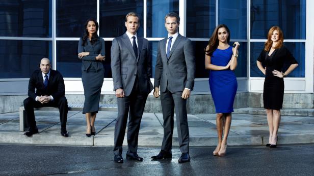 Die Besetzung der Fernsehserie „Suits“ posiert vor einem modernen Gebäude.
