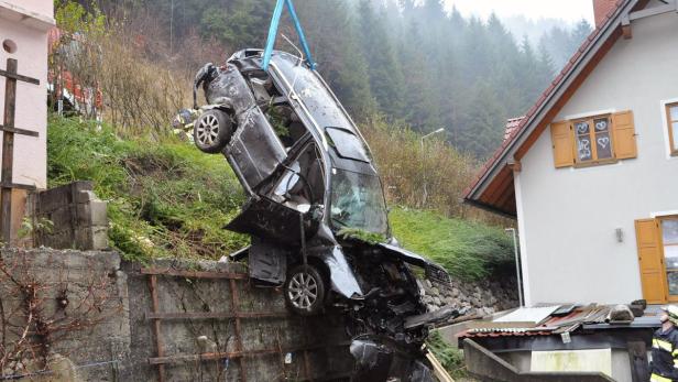 Ein schwarzes Auto hängt beschädigt an einem Kran vor einer Hauswand.