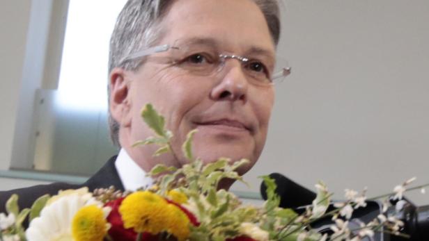 Ein Mann mit Brille steht hinter einem Blumenstrauß und spricht.