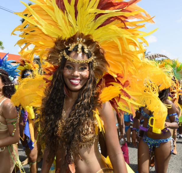 Eine lächelnde Frau mit einem gelb-roten Federkopfschmuck und Karnevalskostüm.