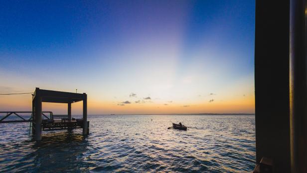 Ein Mann rudert bei Sonnenuntergang in einem kleinen Boot auf dem Meer.