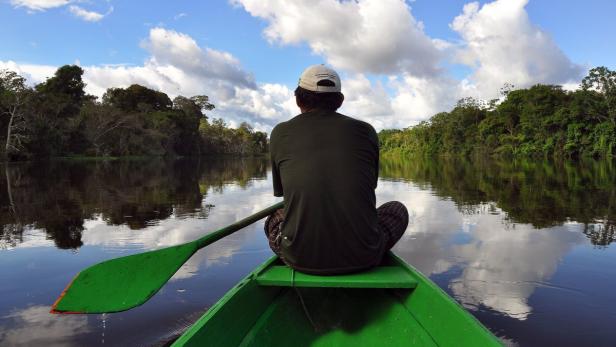 Ein Mann sitzt in einem grünen Boot auf einem Fluss, umgeben von Bäumen.