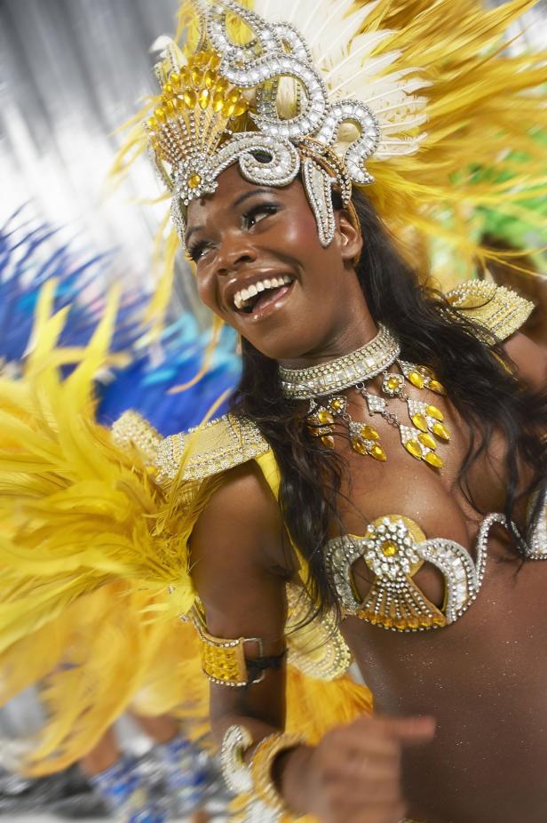 Eine lächelnde Frau in einem gelb-silbernen Karnevalskostüm mit Federn.