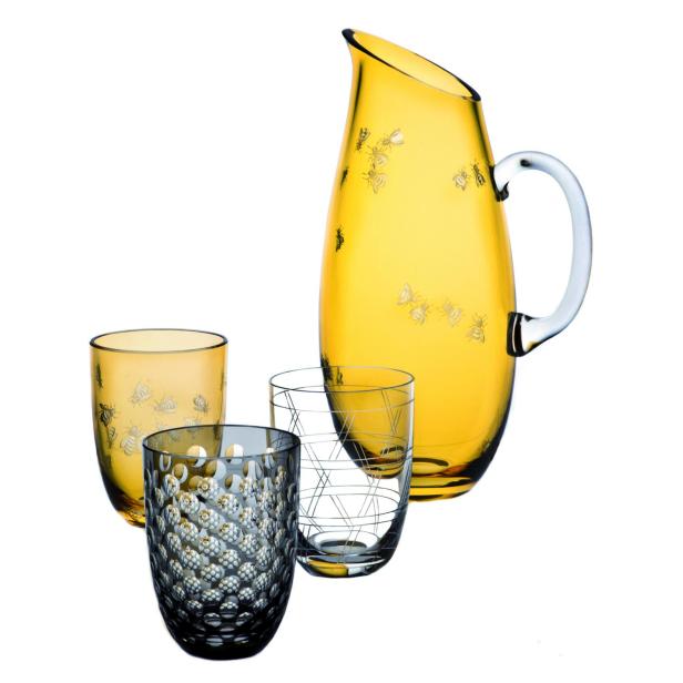 Ein gelber Krug mit Bienendekor steht neben drei Gläsern mit unterschiedlichen Mustern.