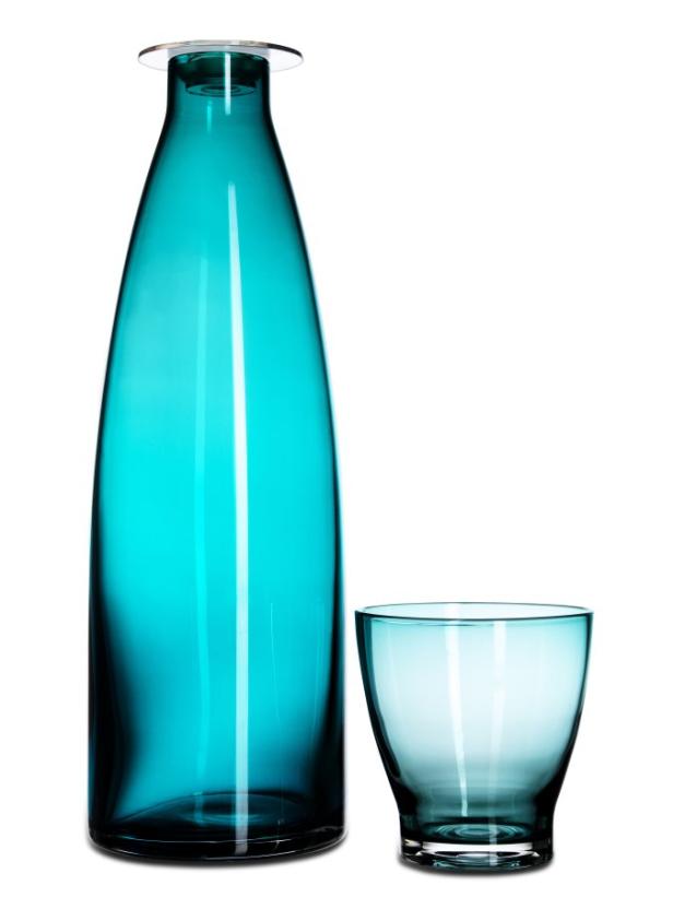 Eine hohe, schlanke, türkisfarbene Glasflasche steht neben einem passenden Glas.