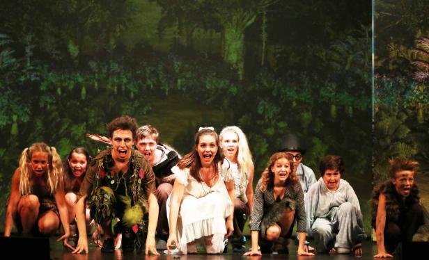 Eine Gruppe von Schauspielern kauert auf einer Bühne vor einem grünen Bühnenbild.