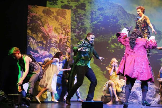 Eine Theaterszene mit Schauspielern in Kostümen vor einem Bühnenbild.