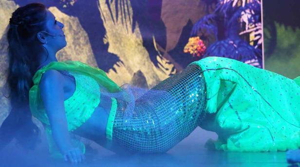 Eine Frau in einem Meerjungfrauenkostüm liegt auf einer Bühne.