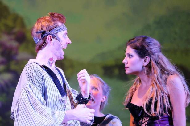 Szene aus einer Theateraufführung mit drei Schauspielern auf der Bühne.