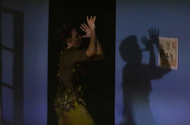 Eine Person in einem Kostüm wirft einen Schatten an eine Wand, an der ein Bild hängt.