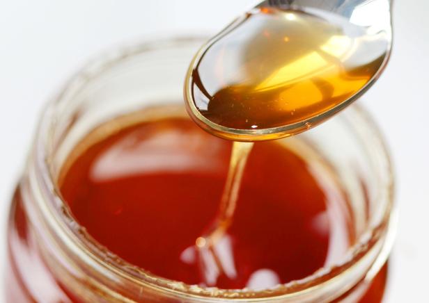 Ein Löffel Honig wird aus einem Honigglas genommen.