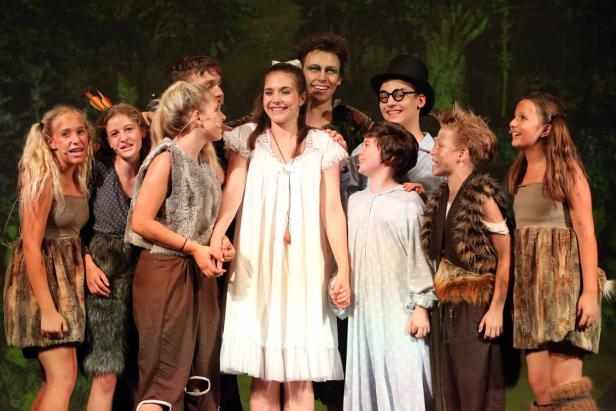 Eine Gruppe von Jugendlichen in Kostümen steht auf einer Bühne vor einem grünen Hintergrund.