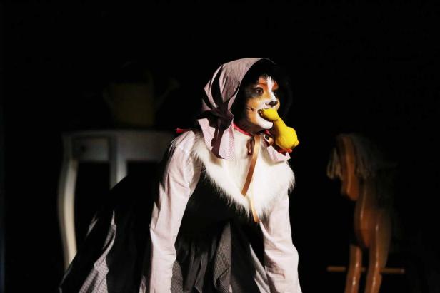 Eine Person in einem Hundekostüm mit Haube hält eine gelbe Quietscheente im Mund.