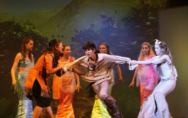Eine Szene aus einem Theaterstück mit einem Jungen in Piratenkleidung und mehreren Mädchen in bunten Kostümen.