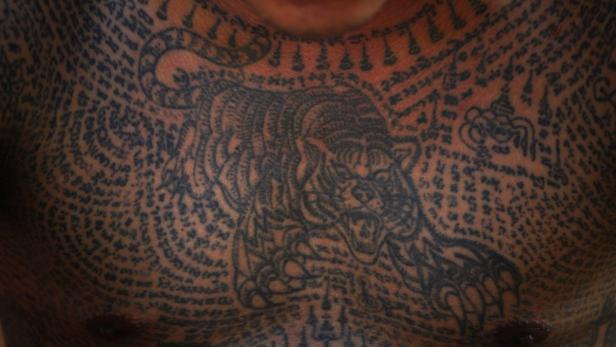 Der Oberkörper einer Person ist mit einem Tiger und thailändischen Schriftzeichen tätowiert.