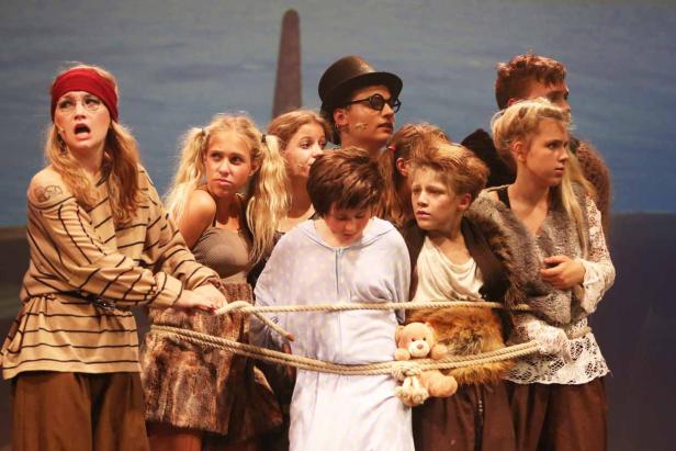 Eine Gruppe von Kindern in Kostümen steht auf einer Bühne und ist mit Seilen gefesselt.