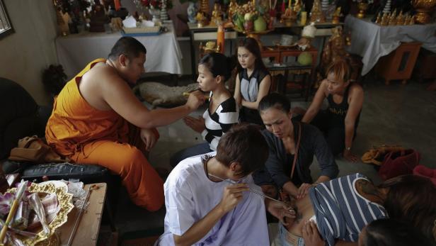 Ein Mönch und andere Personen tätowieren sich in einem Raum mit religiösen Gegenständen.