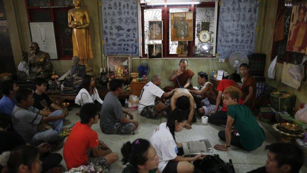 Ein Mönch tätowiert den Rücken eines Mannes, während andere im Raum sitzen.