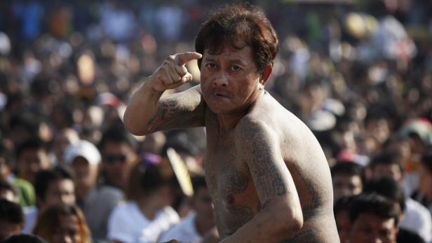 Ein Mann mit Tätowierungen gestikuliert vor einer Menschenmenge.