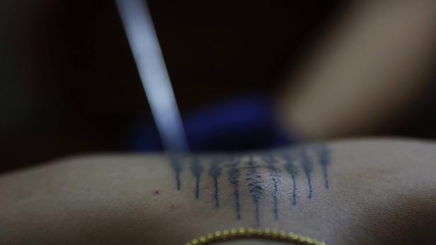 Eine Person erhält ein traditionelles Tattoo auf den Rücken.