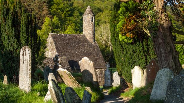 Eine alte Kirche mit einem Rundturm und einem Friedhof im irischen Glendalough.