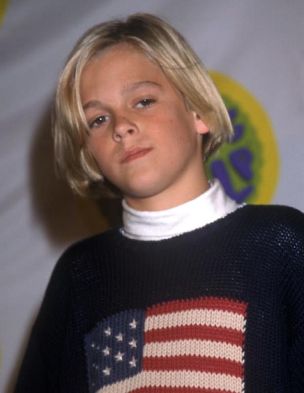 Aaron Carter als junger Mann mit blonden Haaren und einem Pullover mit US-amerikanischer Flagge.