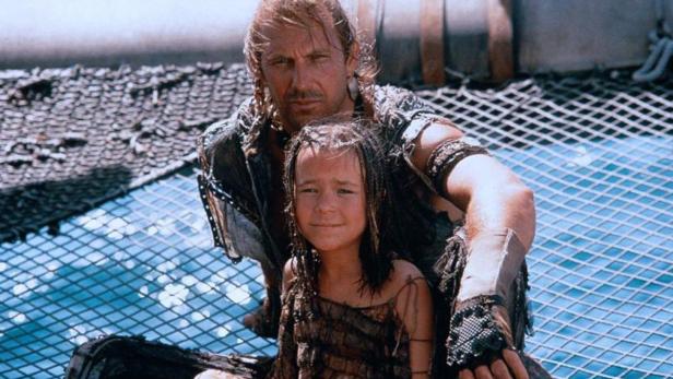 Kevin Costner mit einem Kind auf einem Boot im Film „Waterworld“.