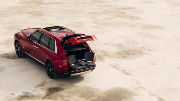 Ein roter Rolls-Royce Cullinan mit geöffneter Heckklappe und ausklappbaren Sitzen.