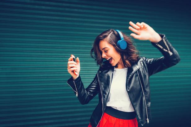 Eine Frau mit Kopfhörern tanzt und hört Musik über ihr Smartphone.