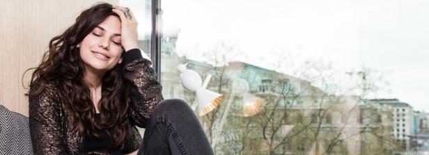 Eine Frau sitzt am Fenster und lächelt mit geschlossenen Augen.