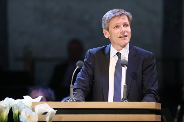 Ein Mann in Anzug und Krawatte steht an einem Rednerpult und spricht.