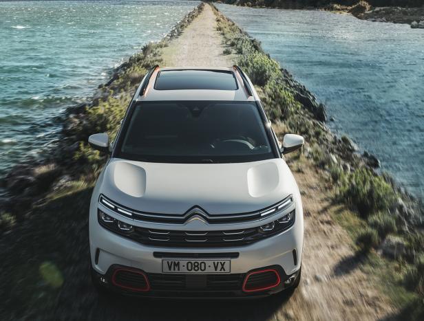 Ein weißer Citroën fährt auf einer schmalen Straße zwischen zwei Gewässern hindurch.