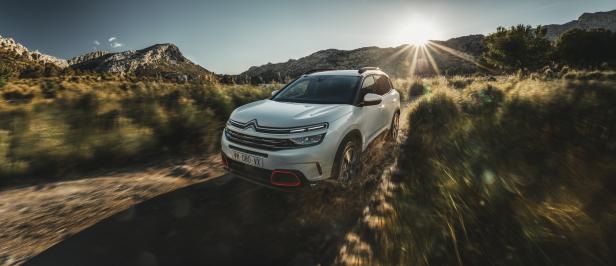 Ein weißer Citroën fährt auf einer unbefestigten Straße in Richtung der Berge.