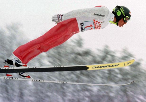 Ein Skispringer in der Luft mit roter Hose und Ski der Marke Atomic.