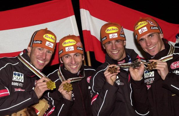 Vier österreichische Skispringer mit Goldmedaillen und Mützen vor der österreichischen Flagge.
