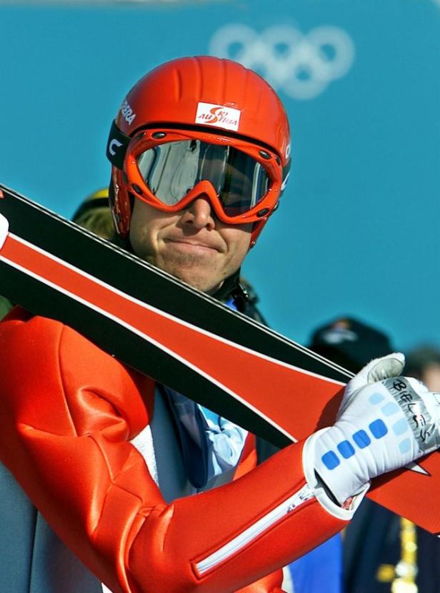 Ein Skispringer mit rotem Helm und Skibrille hält seine Skier.
