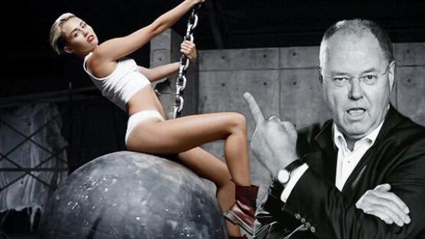 Miley Cyrus posiert auf einer Abrissbirne, während eine Person den Mittelfinger zeigt.