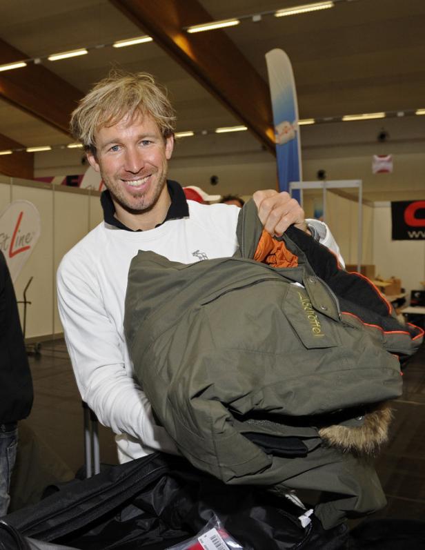 Ein Mann mit blonden Haaren hält eine grüne Winterjacke der Marke Schöffel.
