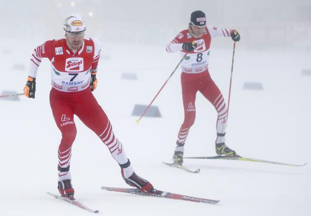 Zwei Skilangläufer in rot-weißer Sportkleidung während eines Wettkampfs im Schnee.