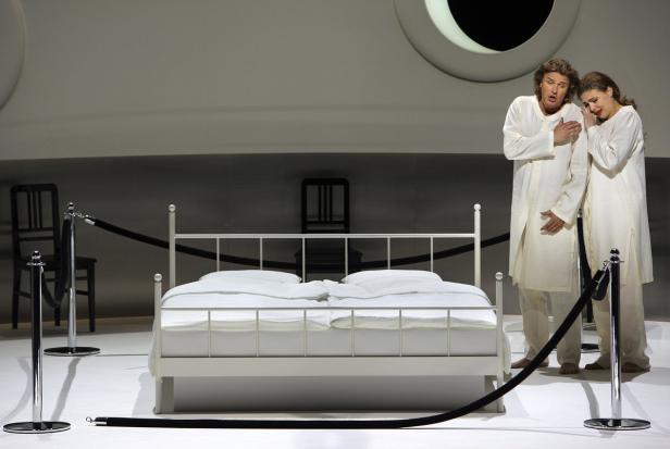 Bayreuther Festspiele 2015 - Lohengrin Zwei Opernsänger stehen in weißen Gewändern neben einem weißen Bett auf der Bühne.